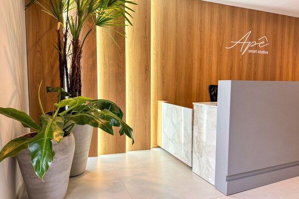 A reception area with a wooden wall, marble reception desk, and large potted plants. - Apê Pátio Paulista  (São Paulo)