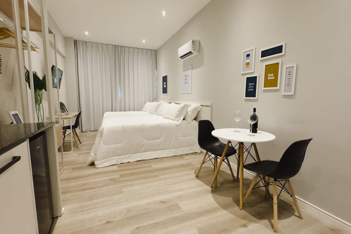 Ett modernt hotellrum med en säng, ett skrivbord, en stol, ett litet bord med ett vinglas och konst på väggen.