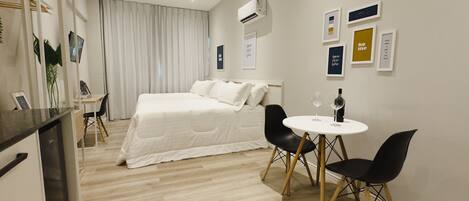 Una habitación de hotel moderna con una cama, un escritorio, una silla, una mesita con una copa de vino y decoración en la pared.