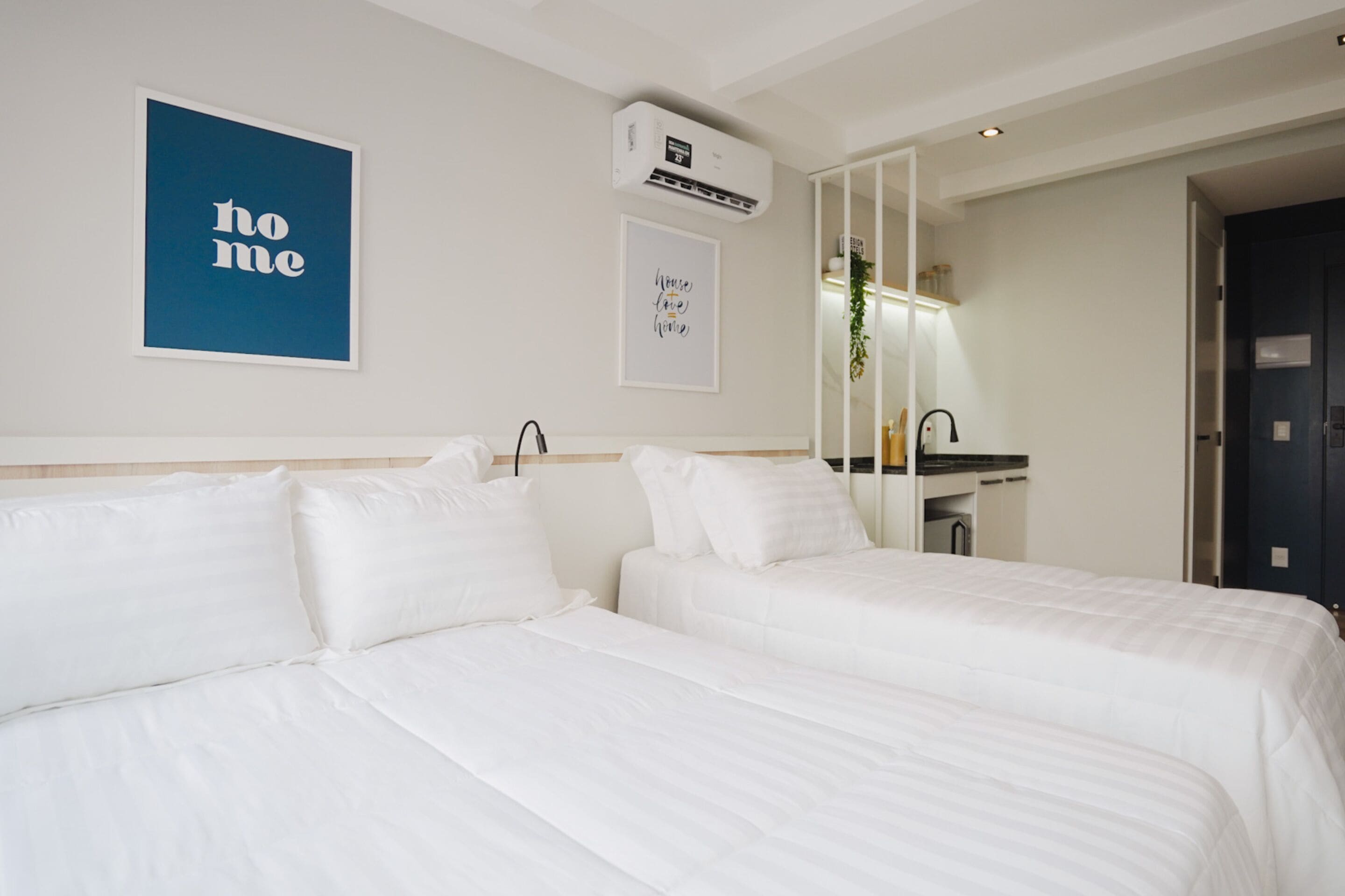 Une chambre d’hôtel avec deux lits, un grand miroir, un climatiseur fixé au mur et une pancarte indiquant « chez soi ».