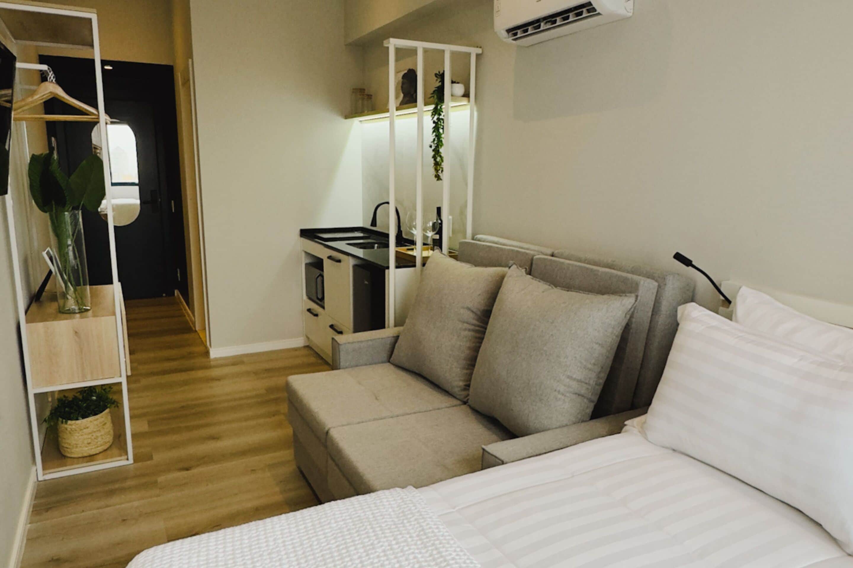 Ein modernes Hotelzimmer mit Bett, einer Sitzecke, einer kleinen Küchenzeile und einem begehbaren Kleiderschrank.