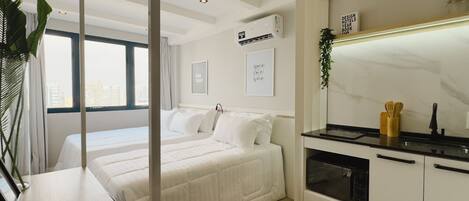 A modern hotel room with a large bed, a kitchenette, and a city view.