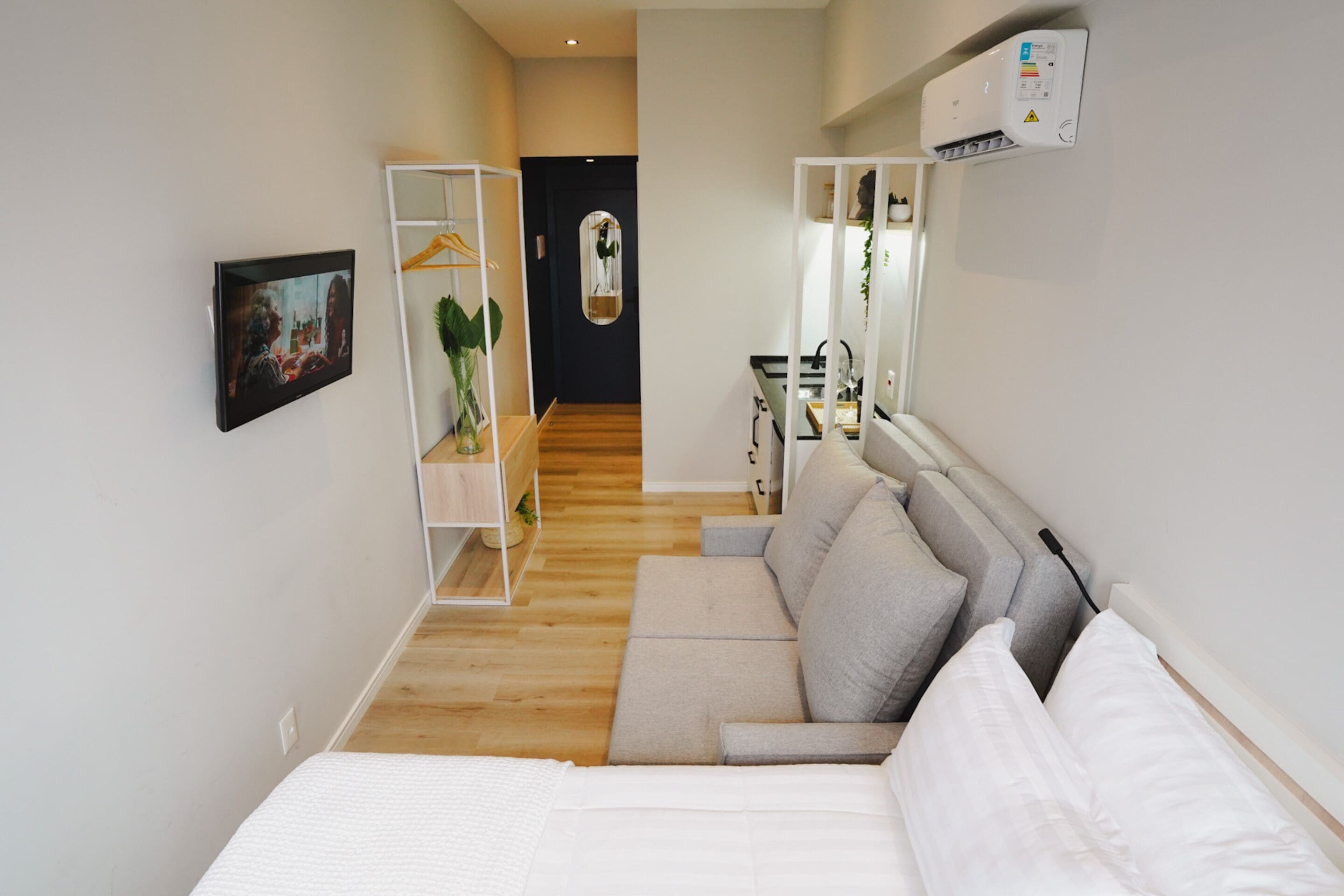 A modern hotel room with a bed, a sofa, a small desk, and a wardrobe.