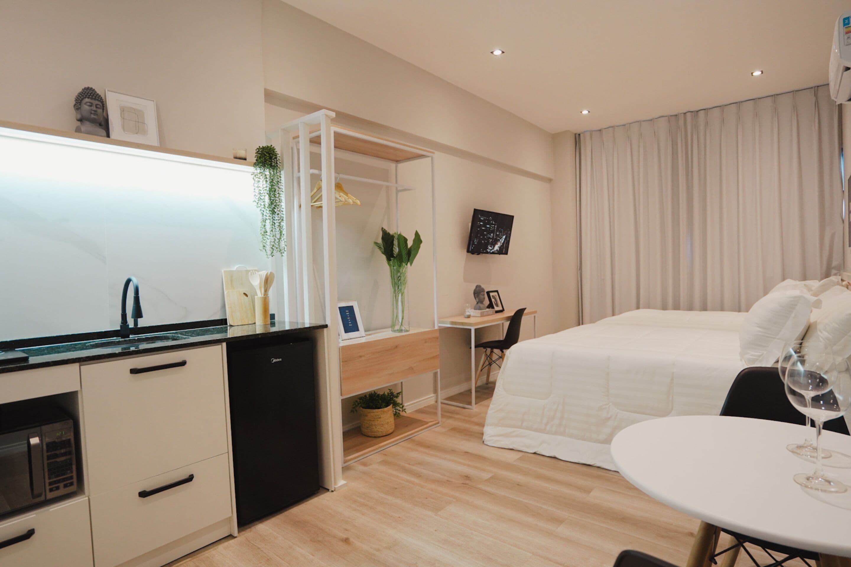 A modern hotel room with a kitchenette, a bed, a desk, and a TV.