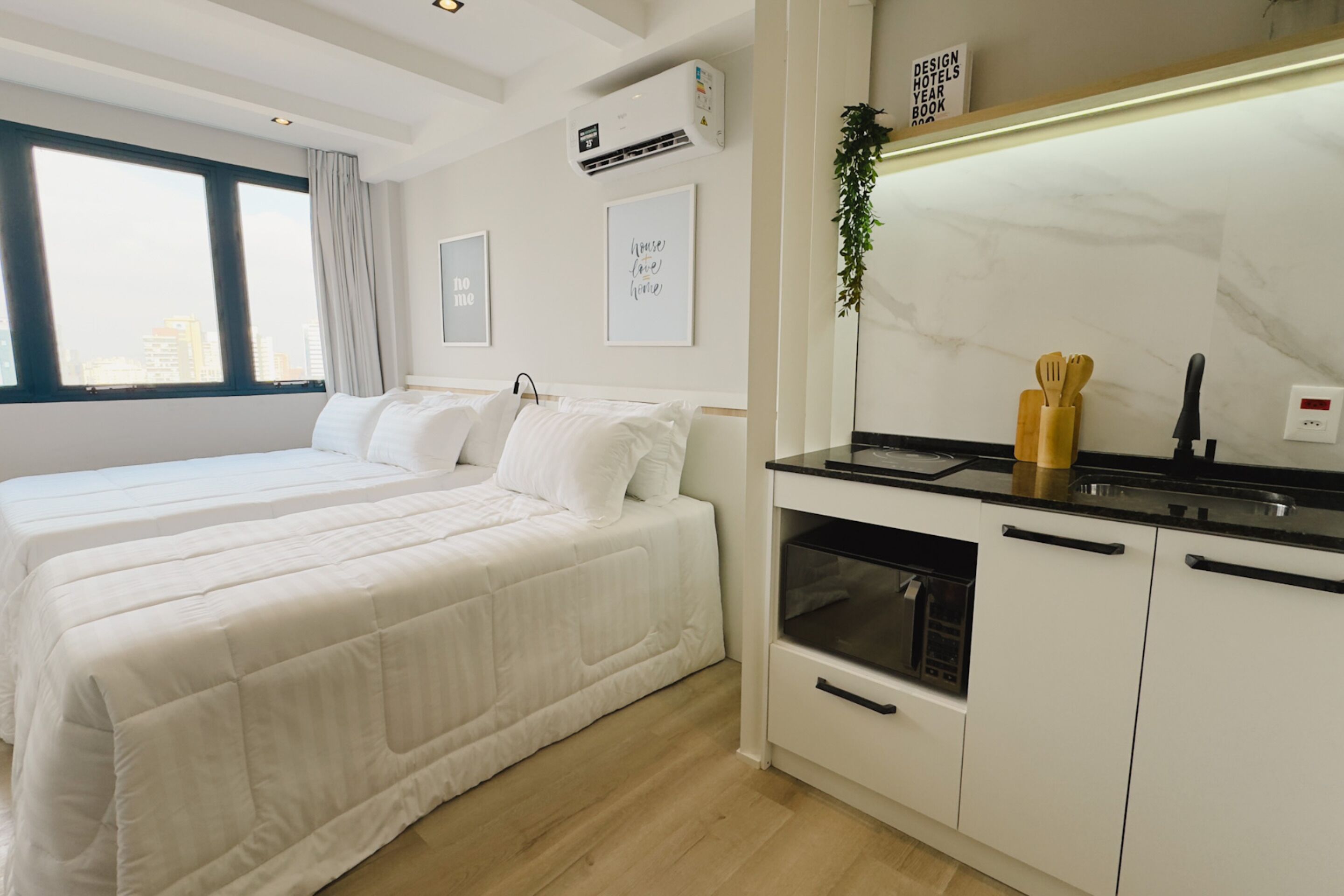 A modern hotel room with a large bed, a kitchenette, and a view of the city.