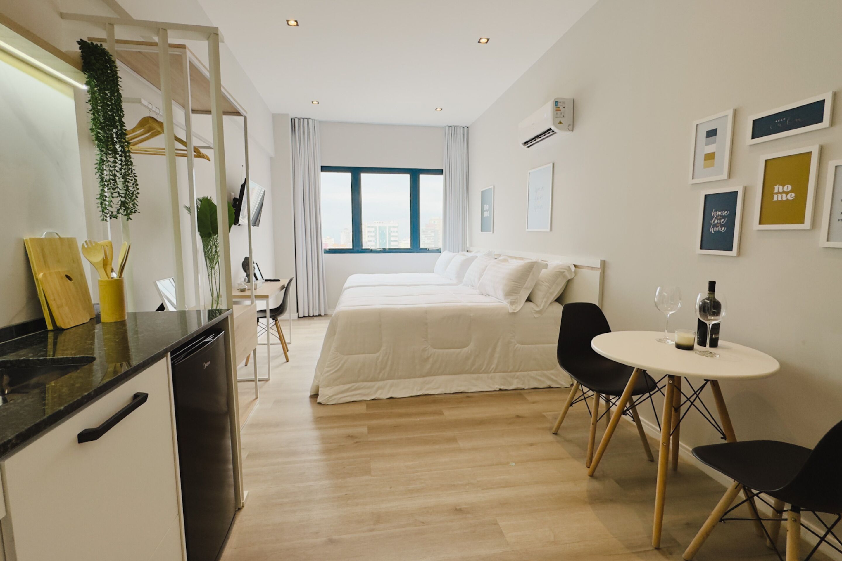 A modern hotel room with a bed, a dining area, and a kitchen.