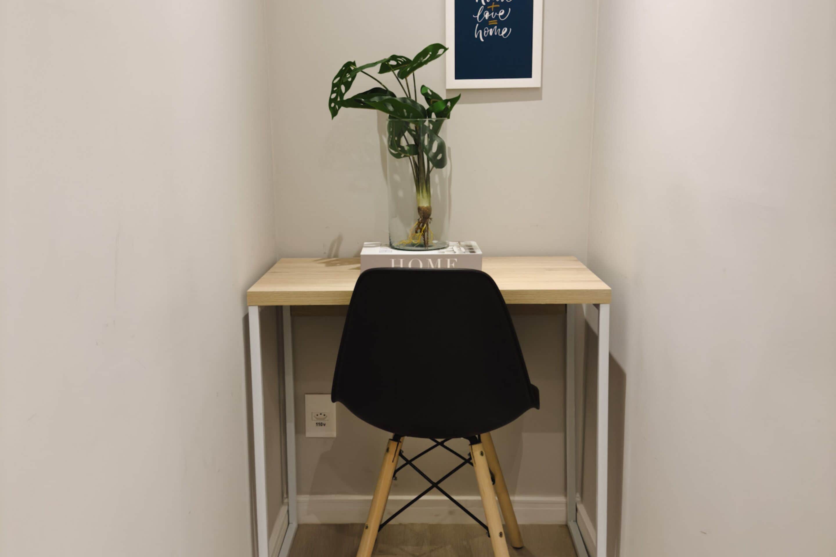 Un espacio de trabajo pequeño con un escritorio de madera, una silla negra y una planta en maceta.