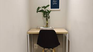 Un espacio de trabajo pequeño con un escritorio de madera, una silla negra y una planta en maceta.