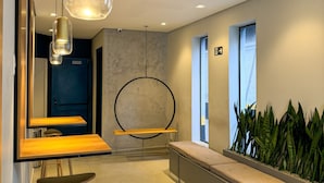 Un espace d’accueil moderne avec un comptoir de réception en bois, une étagère ronde noire, un banc et une plante en pot.