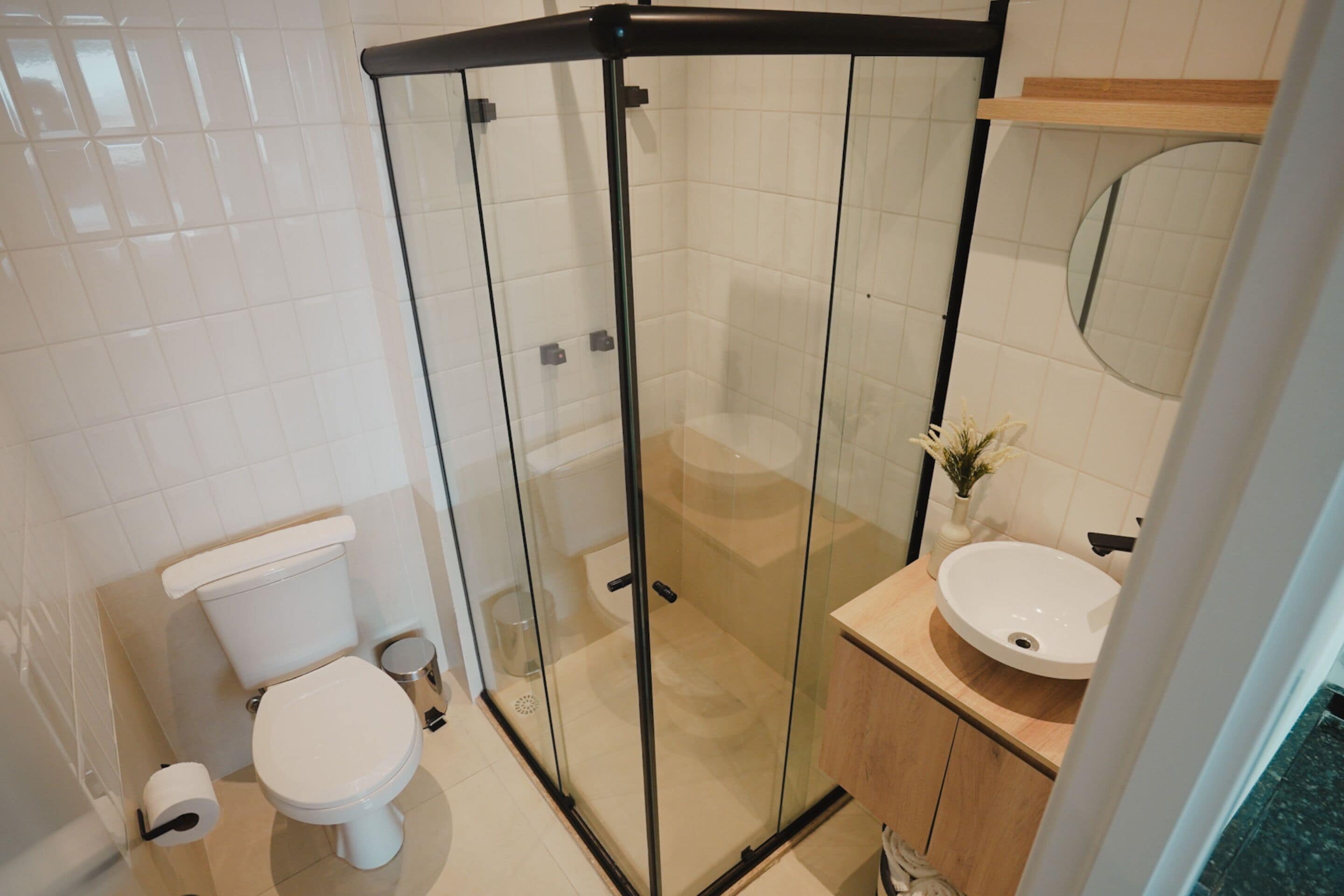 Een moderne badkamer met een glazen douchecabine, een toilet en een wastafel met spiegel.