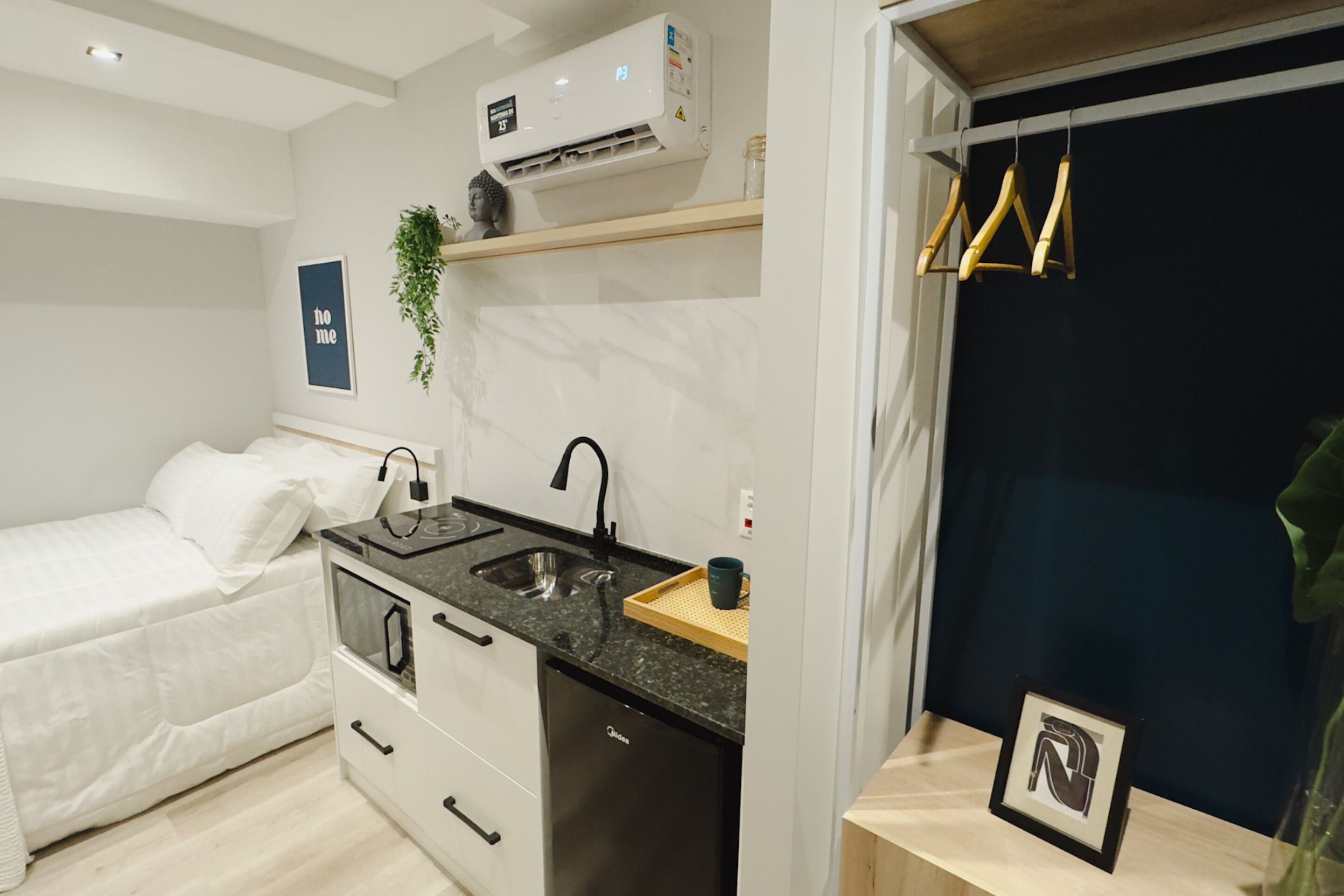 A compact bedroom with a bed, a small kitchenette with a sink, and an air conditioning unit.
