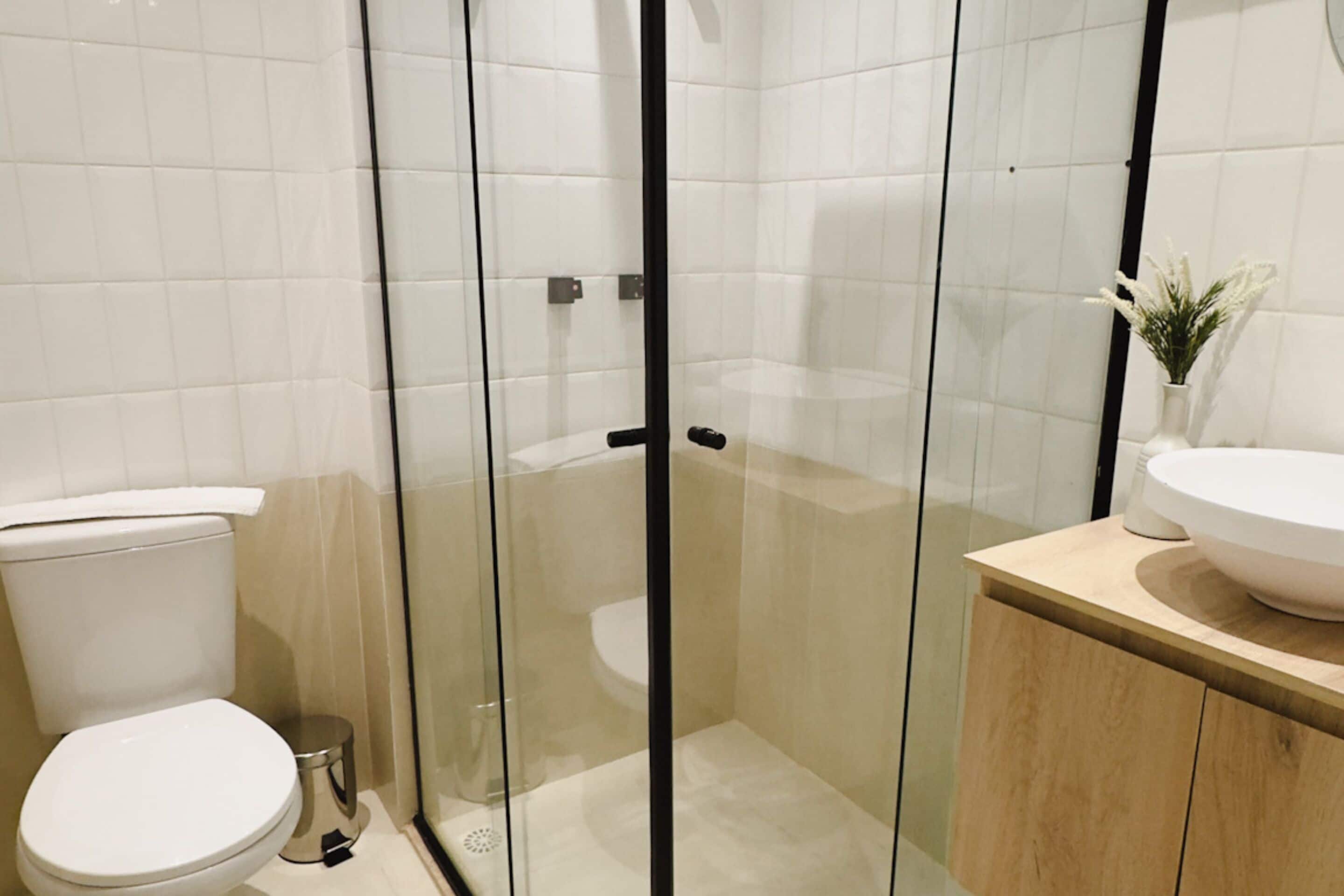 Ein modernes Badezimmer mit einer Duschkabine aus Glas, einer weißen Toilette und einem Holzwaschtisch mit großem Becken.