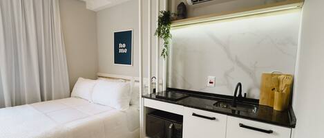 Une chambre compacte comprenant un lit, une petite kitchenette équipée d’un four à micro-ondes et un évier.
