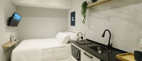 A compact bedroom with a bed, bedside table, and a TV mounted on the wall.