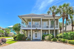 A two-story building with a balcony, surrounded by palm trees and greenery.