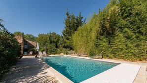 Ein rechteckiger Pool mit Holzterrasse, umgeben von üppiger Vegetation und Bäumen.