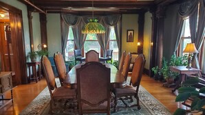 Uma sala de jantar formal com uma grande mesa de madeira, cadeiras ornamentadas e um tapete estampado.