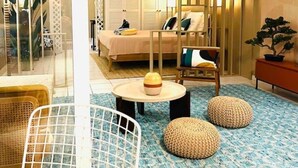 A hotel room with a bed, a chair, a small table with a bowl, and a potted plant.