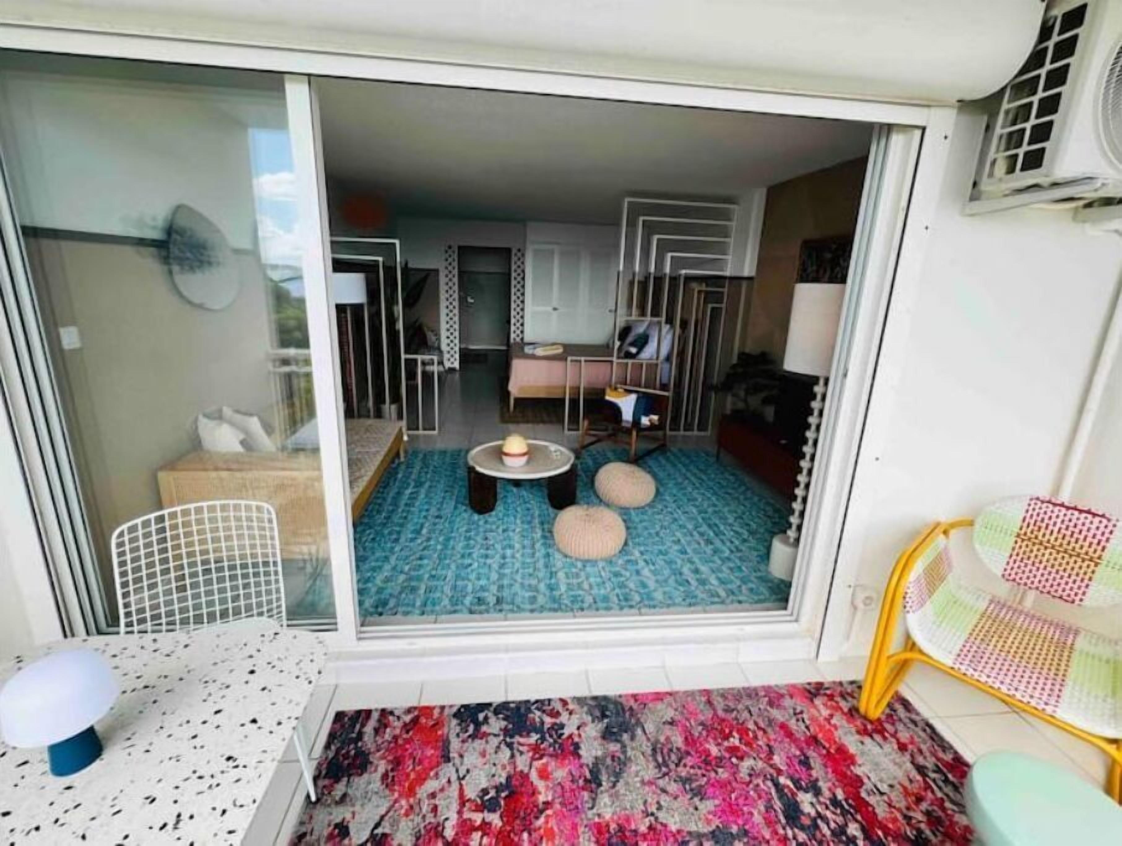A balcony with a blue patterned floor, a white table with a blue base, a white chair, and a colorful rug.