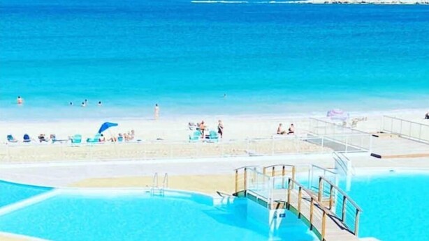 A pool area with a clear view of the ocean and beach.