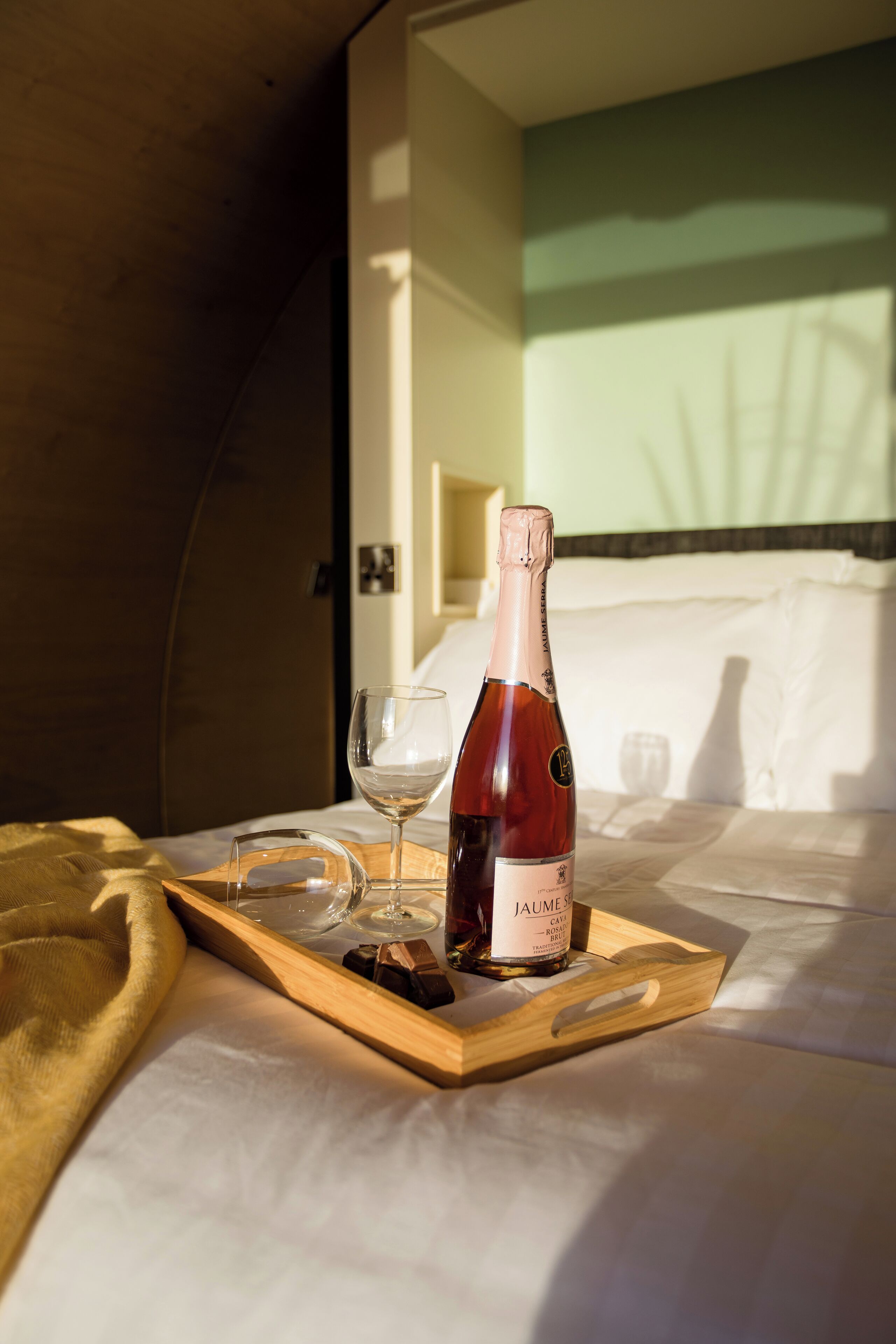 Une table de chevet en bois sur laquelle se trouvent une bouteille de champagne, un verre et une bouteille d’eau.