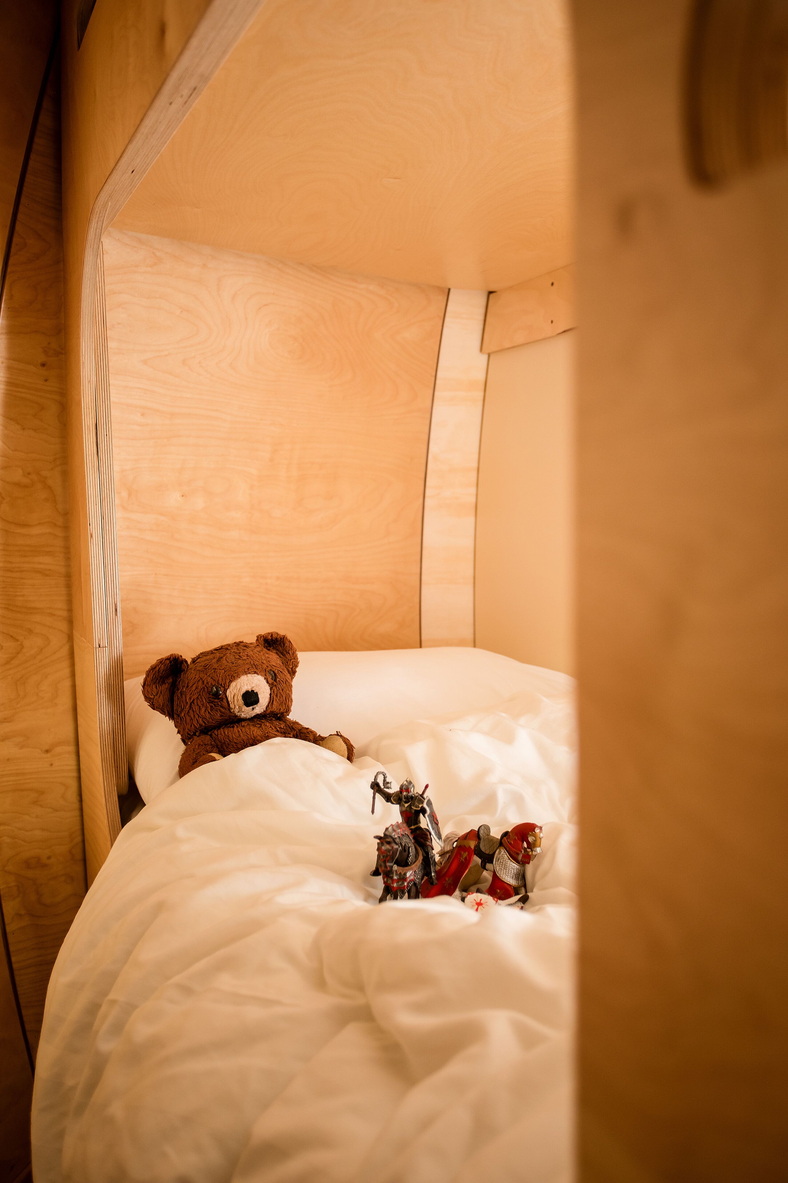 Un letto a castello in legno con un orsacchiotto e soldatini giocattolo sul materasso.