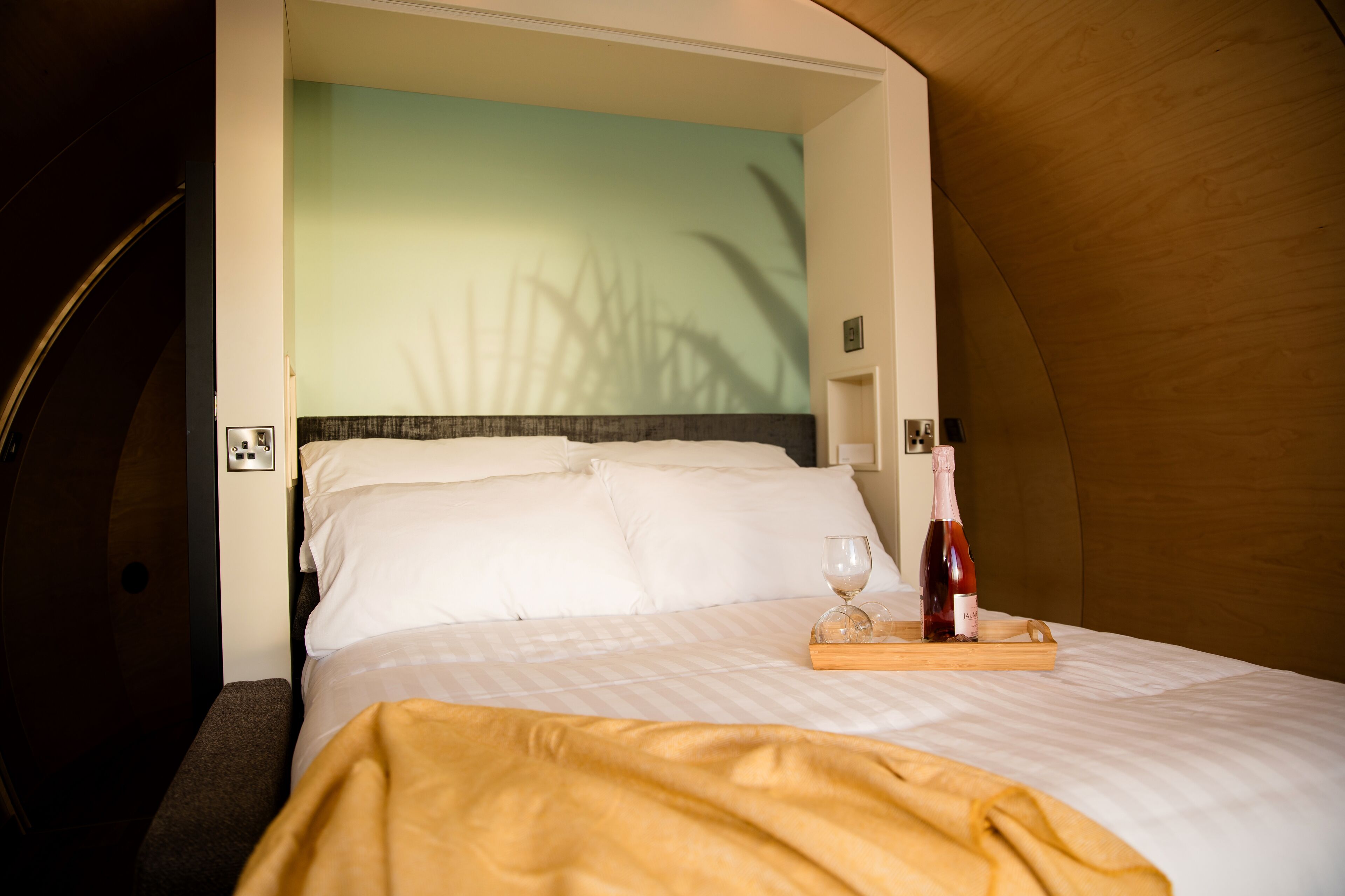 A bed with white linens, a wooden headboard, and a bedside table with a bottle and glass.