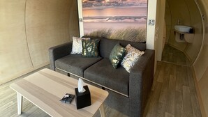 Une pièce chaleureuse avec un canapé gris, une petite table et un tableau représentant un coucher de soleil sur la mer.