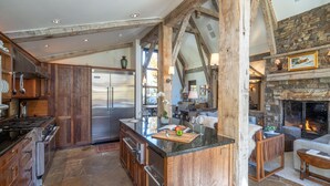 A spacious kitchen with a large island, wooden beams, stone flooring, and a stone fireplace. - Mountain House by Exceptional Stays (Mountain Village)