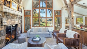 A spacious living room with a stone fireplace, large windows, and a cozy seating area. - Mountain House by Exceptional Stays (Mountain Village)