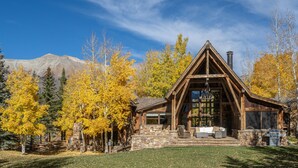 A log cabin with a stone foundation, large windows, and a chimney. - Mountain House by Exceptional Stays (Mountain Village)