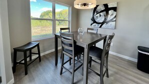A dining area with a table and chairs, a hanging light fixture, and a large window with a view of greenery.