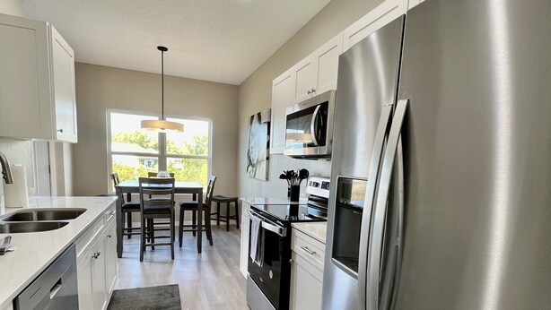 A modern kitchen with stainless steel appliances, a dining area with a view, and a large refrigerator.