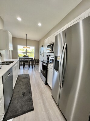 A modern kitchen with stainless steel appliances, a dining area with a view, and a large refrigerator. - Cedar Falls Townhome - New Construction - 3 KING BEDS! (Cedar Falls)