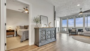 A spacious living area with a large window, a wooden floor, and a grey cabinet with decorative items. - Good Vibes Only in the Stillwater at Bridges Bay Resort (Arnolds Park)