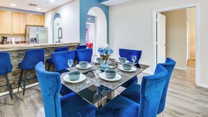 A dining area with a glass-top table, blue chairs, and a kitchen in the background. - 2 Mi to Animal Kingdom: Kissimmee Resort Condo! (Kissimmee)