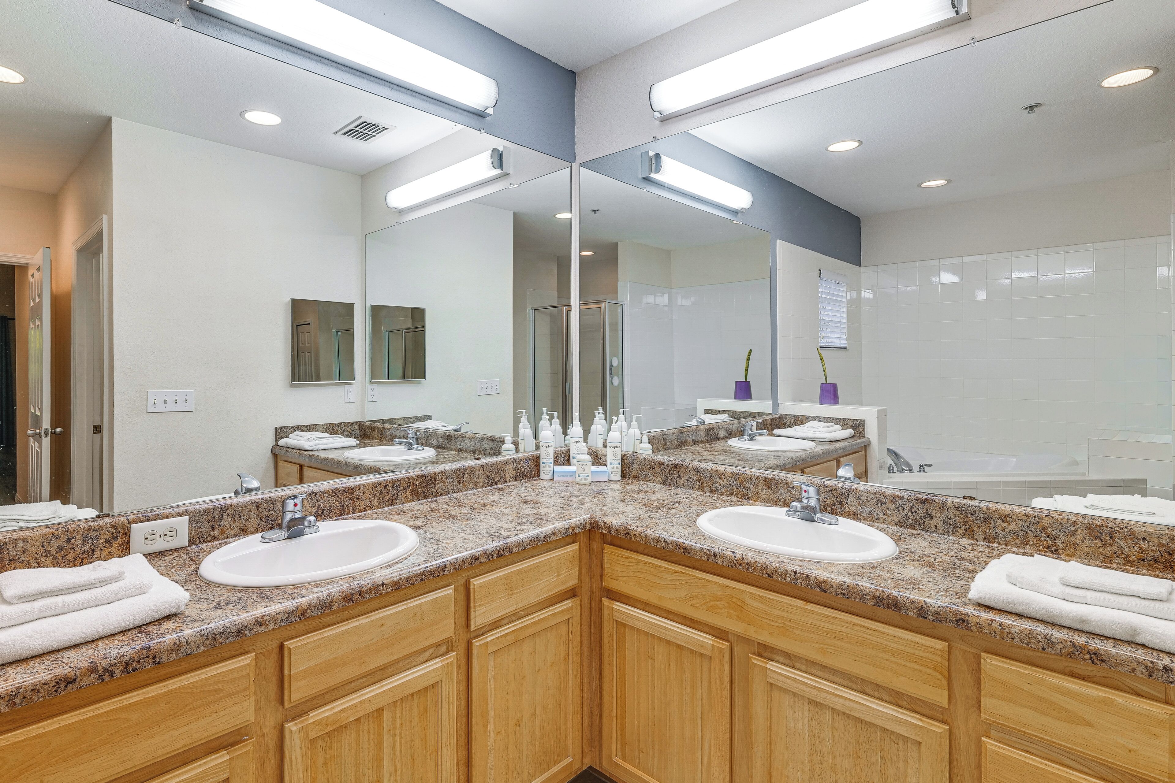 A modern bathroom with granite countertops, dual sinks, wooden cabinets, and a large mirror.