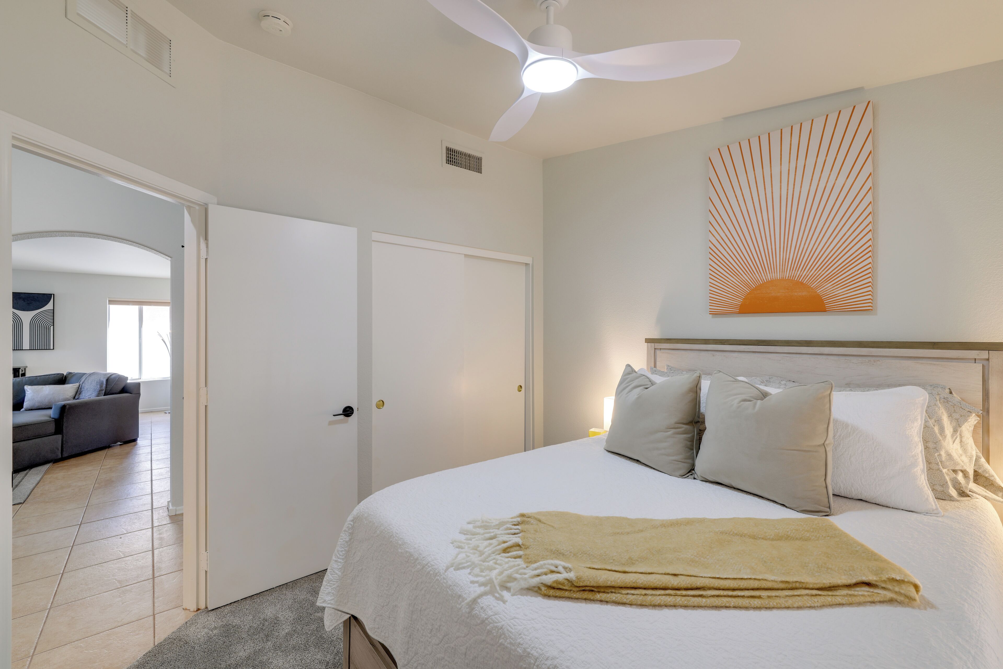 A bedroom with a bed, a ceiling fan, a wall-mounted artwork, and a door leading to another room.