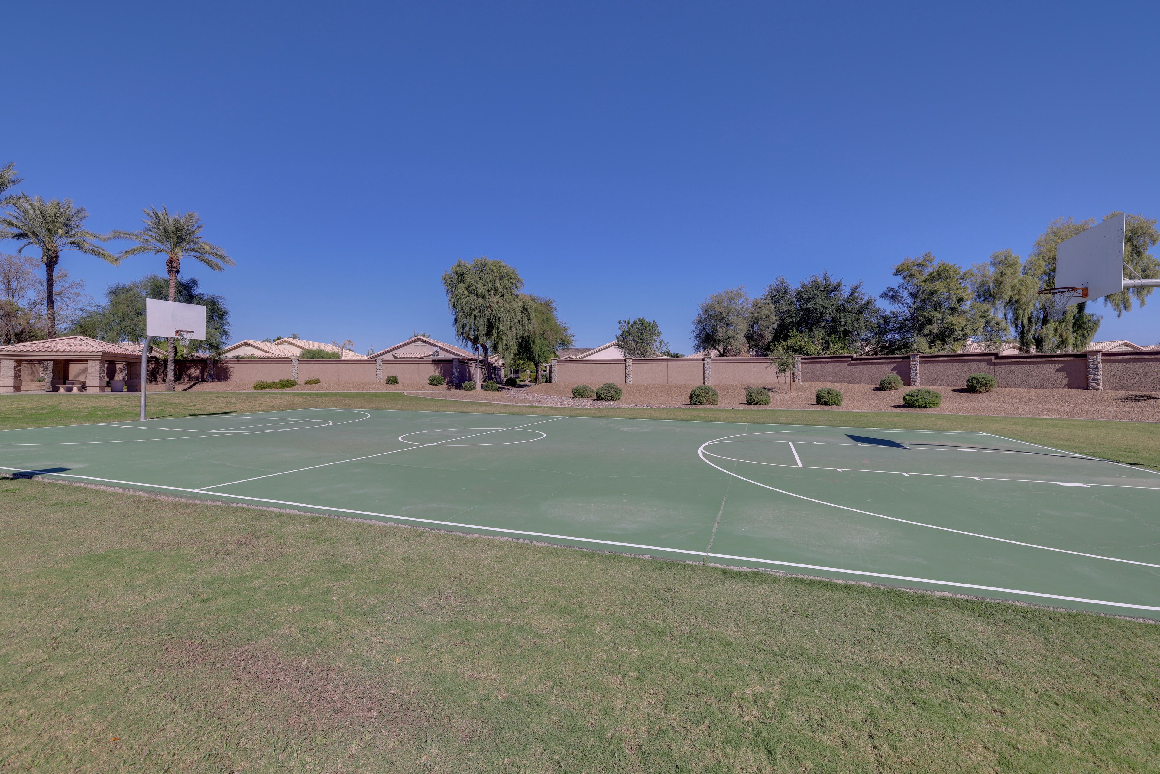 A basketball court with a clear sky, surrounded by houses and palm trees.