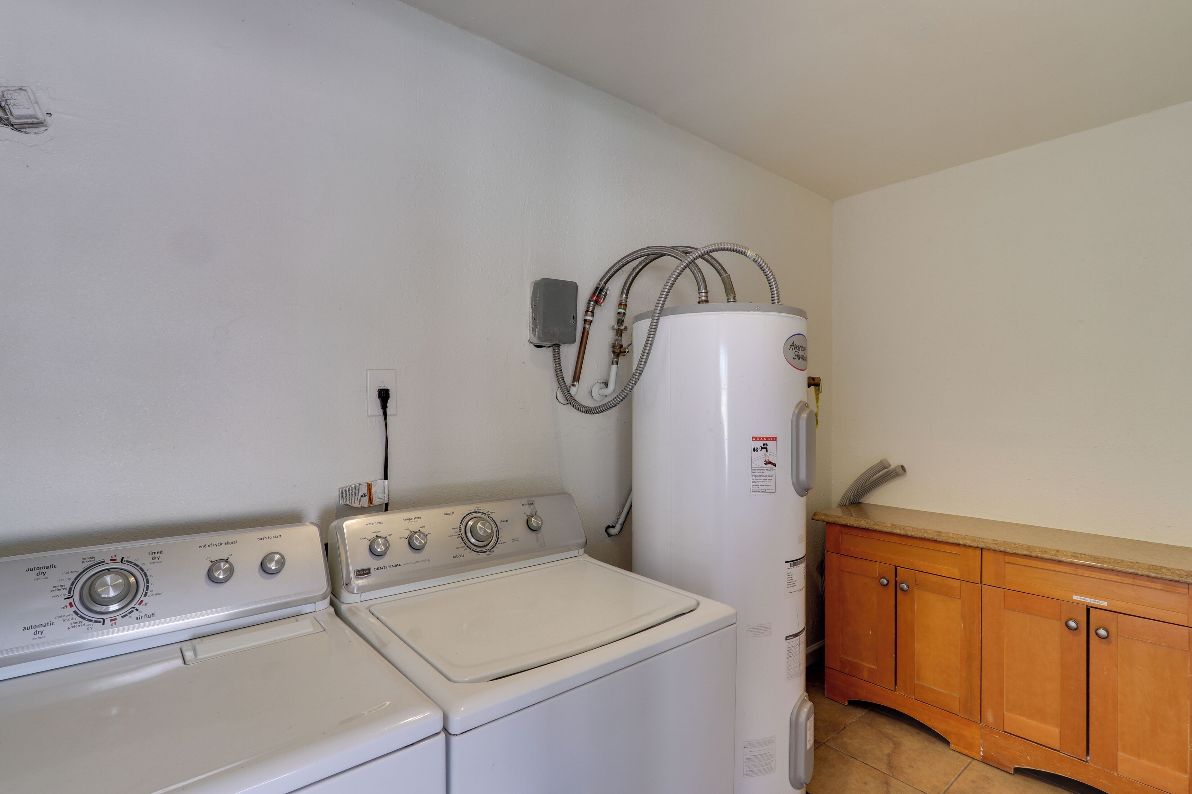 A laundry area with two washing machines and a dryer, a wooden cabinet, and a wall-mounted heater.
