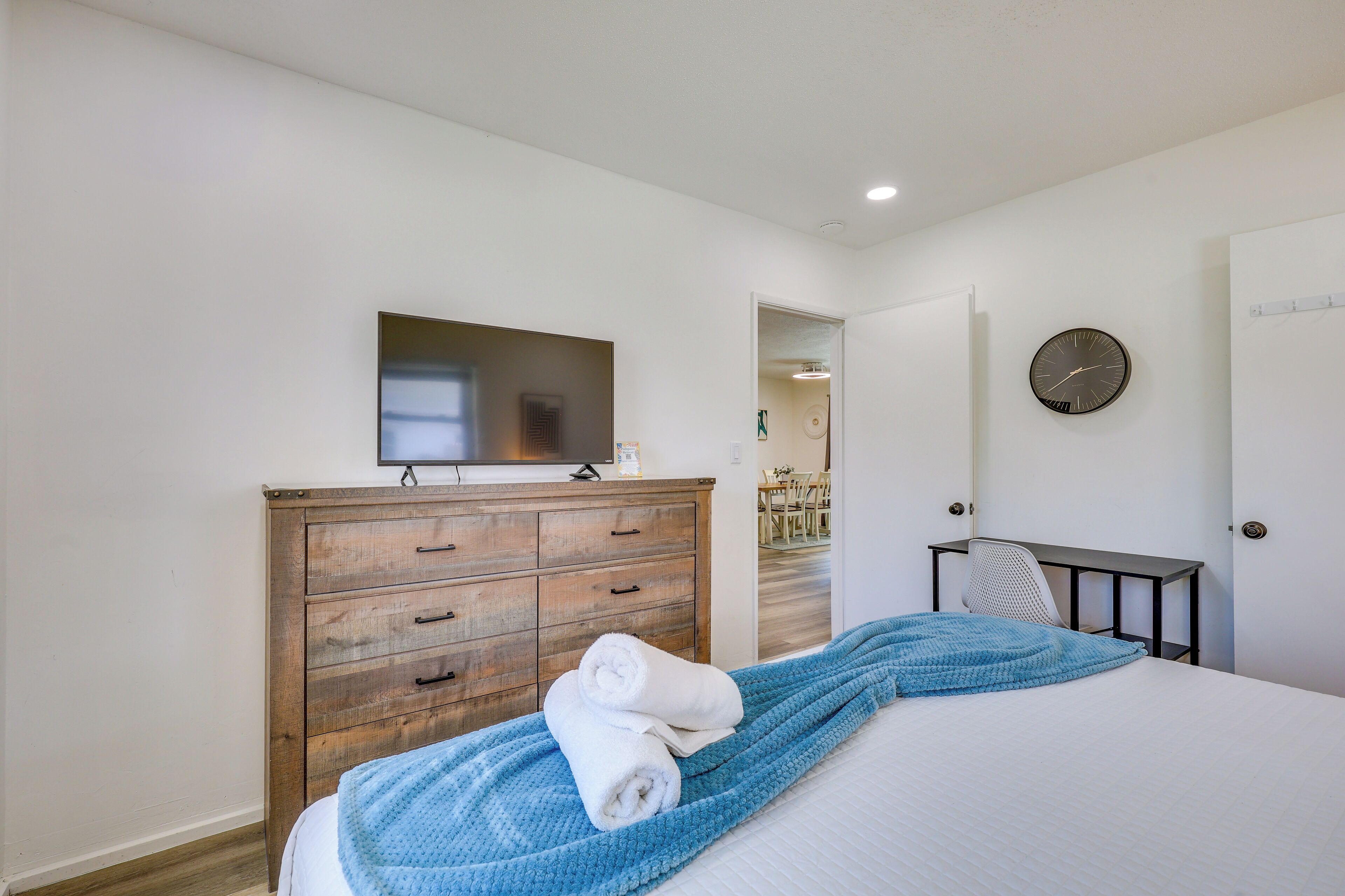 A bedroom with a bed, a wooden dresser, a desk, a chair, a clock, and a mirror.