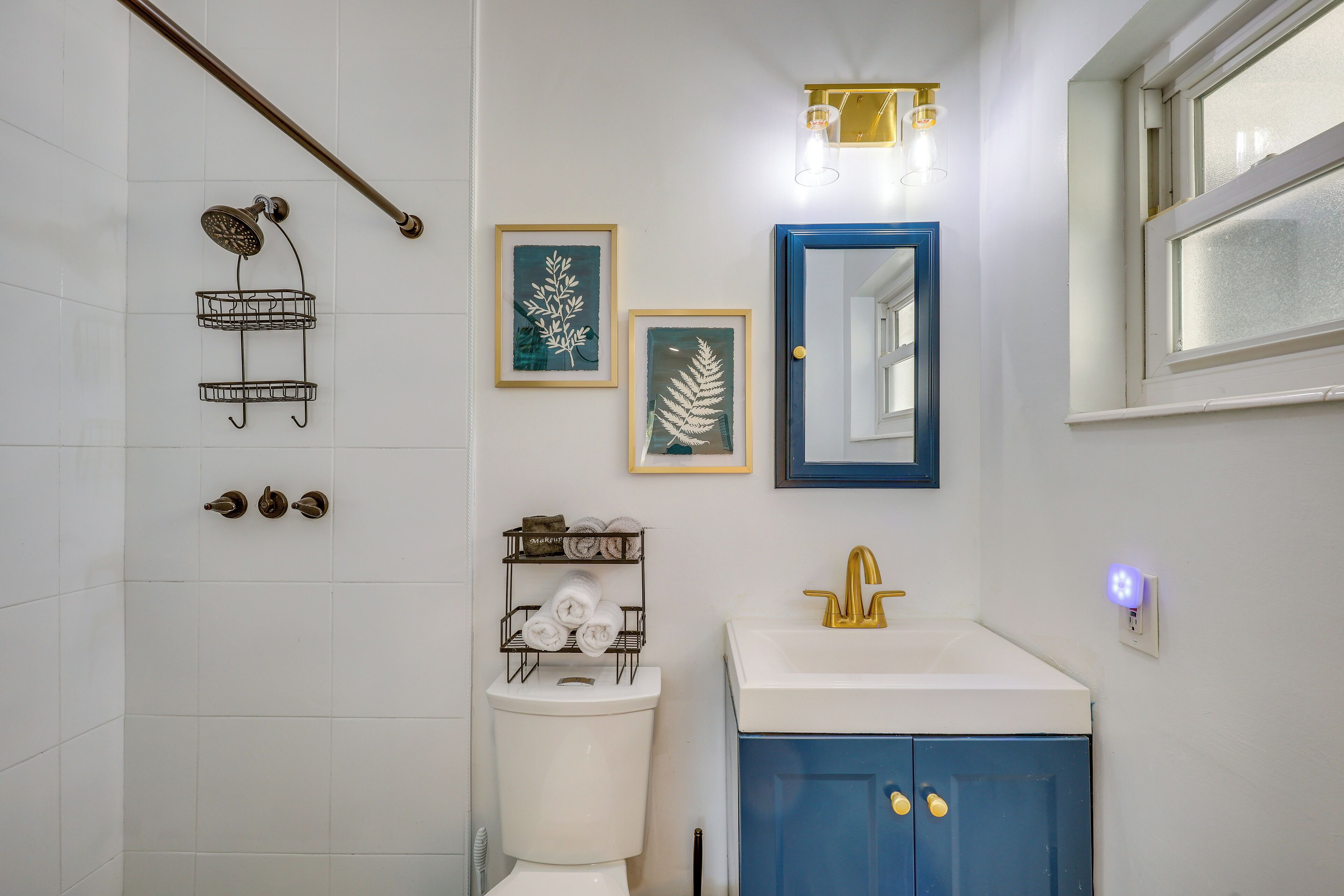 Une salle de bain équipée d’une douche, de toilettes, d’un lavabo et ornée d’œuvres d’art encadrées au mur.