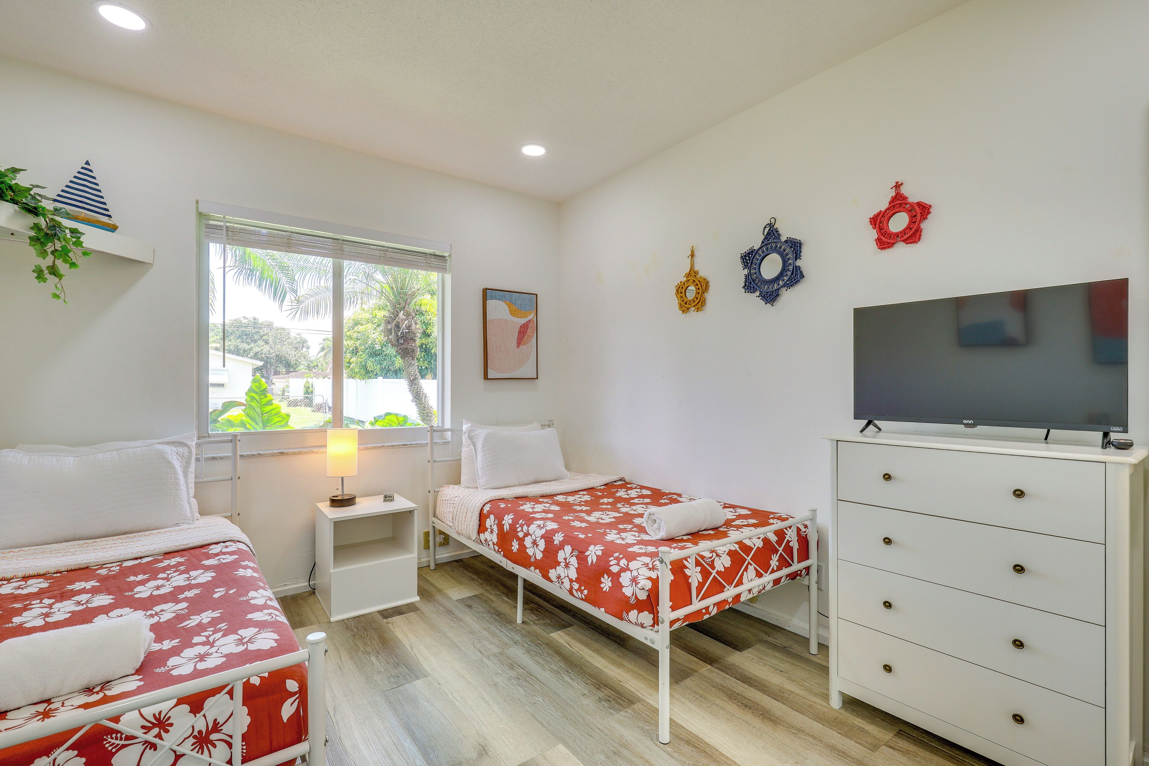 Une chambre avec deux lits, une télévision, une commode, une fenêtre donnant sur un paysage agréable et des éléments décoratifs sur les murs.