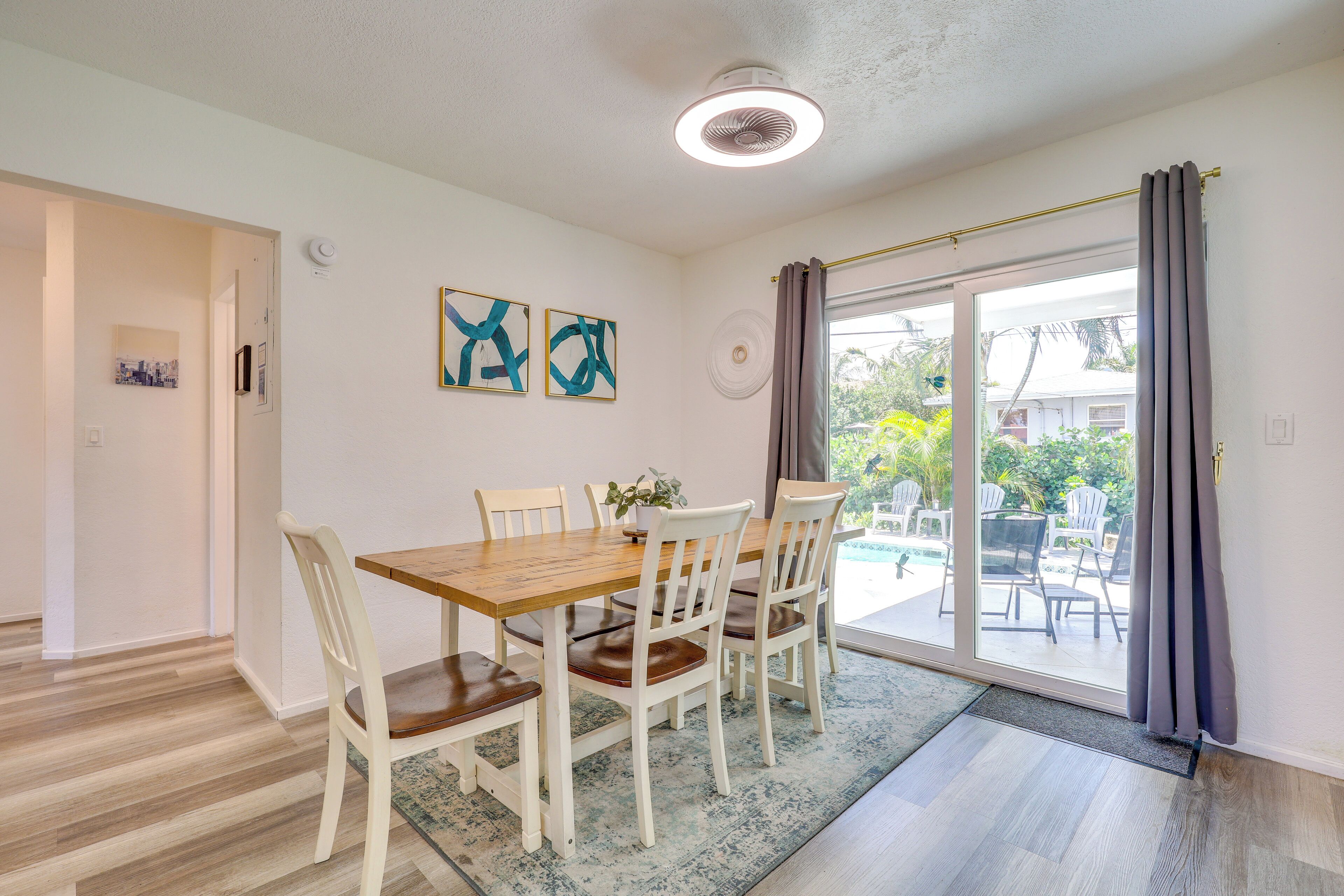 A dining area with a wooden table and white chairs, a ceiling fan, and a view through a glass door to an outdoor patio.