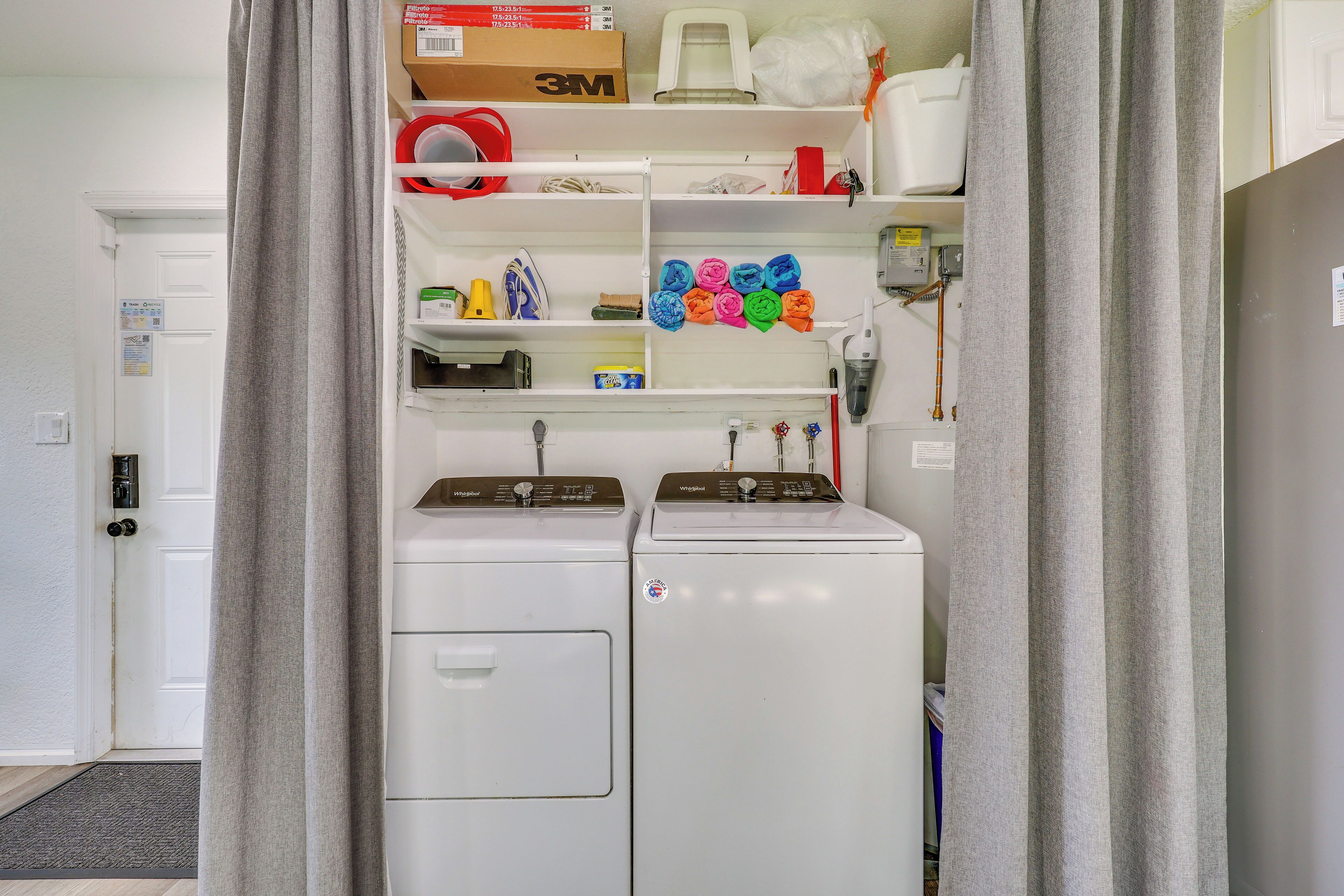 A laundry room with two stacked washers and dryers, shelves with various items, and a door leading to another room.