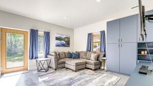 A modern living room with a sectional sofa, a small table, and a large window with curtains. - Unique Grand Junction Guest Suite w/ Gas Fire Pit! (Grand Junction)