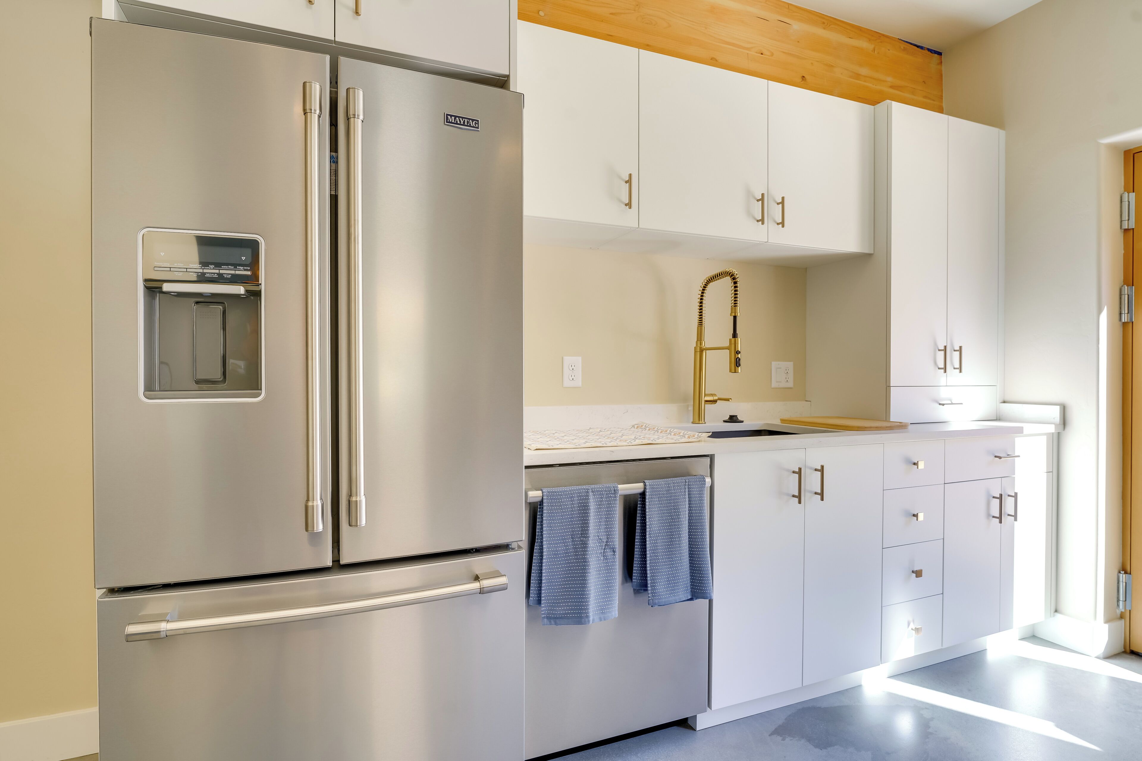 A modern kitchen with stainless steel appliances, white cabinetry, and a wooden ceiling.