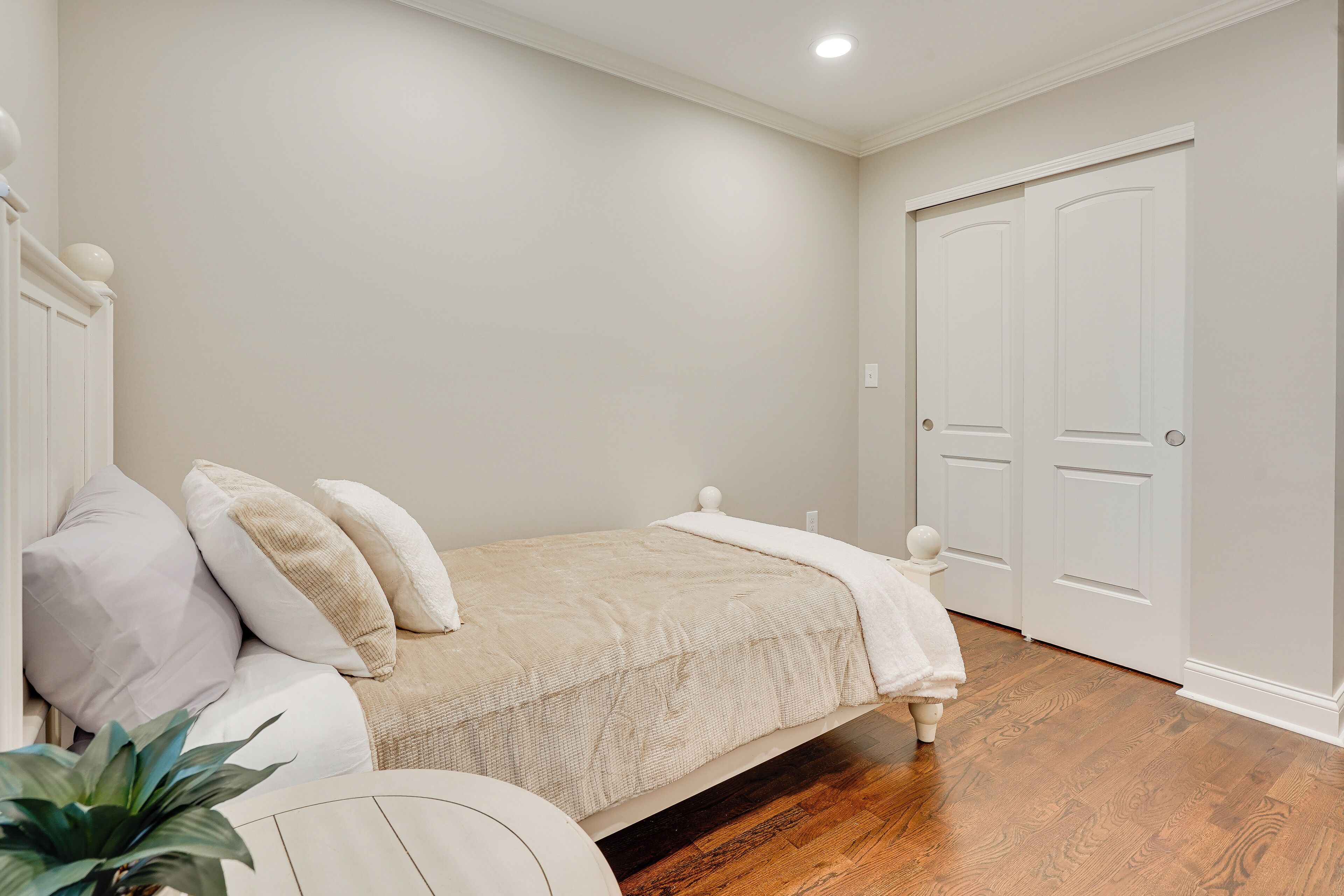 A bedroom with a bed, white walls, a wooden floor, and a white door.