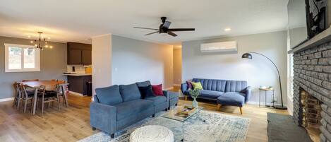 A modern living room with a sofa, coffee table, and ottoman, a dining area with a table and chairs, and a fireplace.