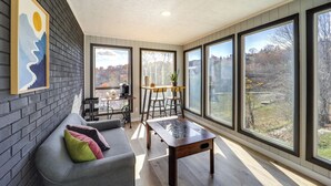 A modern living room with a gray sofa, a wooden coffee table, and large windows offering a view of a wooded area. - Pet-friendly Boone Home w/ Scenic Mountain Views! (Boone)